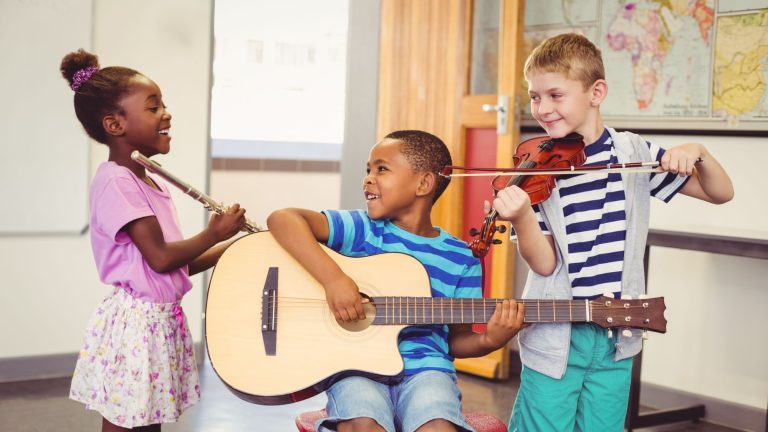 Smiling,Kids,Playing,Guitar,,Violin,,Flute,In,Classroom,At,School